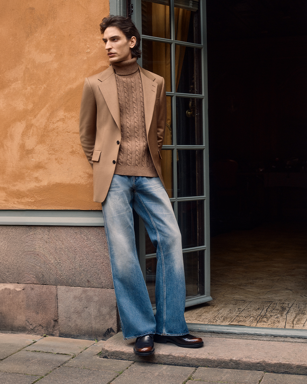 Man in beige blazer & cableknit turtleneck and blue jeans